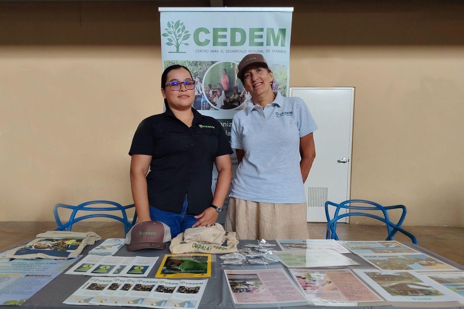 Two CEDEM representatives standing behind a table with brochures, hats, and educational materials during Panama Wildlife Conservation’s Festival de las Guacamayas.